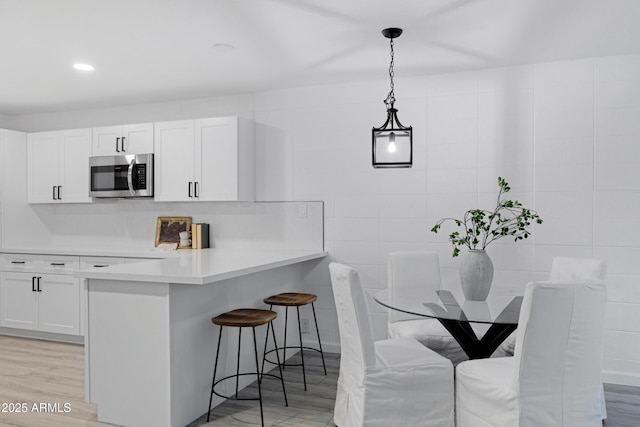 kitchen with white cabinets, a kitchen breakfast bar, tile walls, hanging light fixtures, and light hardwood / wood-style flooring