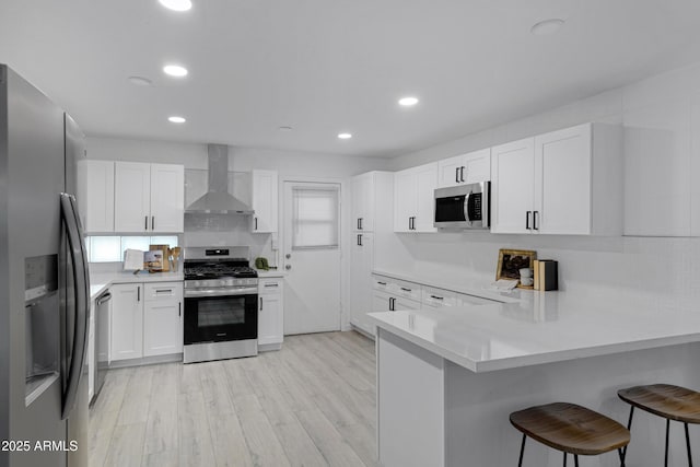 kitchen with a kitchen breakfast bar, wall chimney range hood, white cabinets, kitchen peninsula, and stainless steel appliances