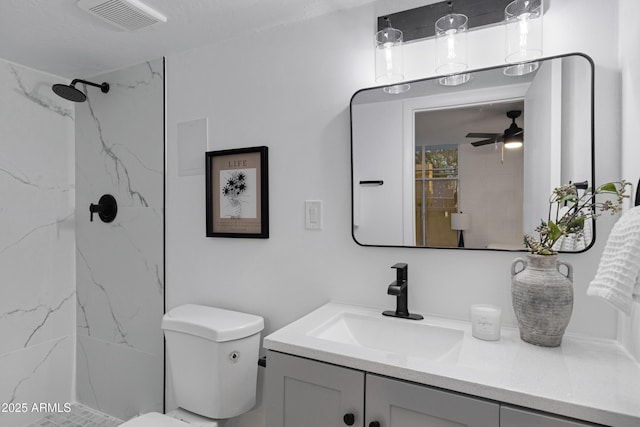 bathroom with tiled shower, toilet, ceiling fan, and vanity