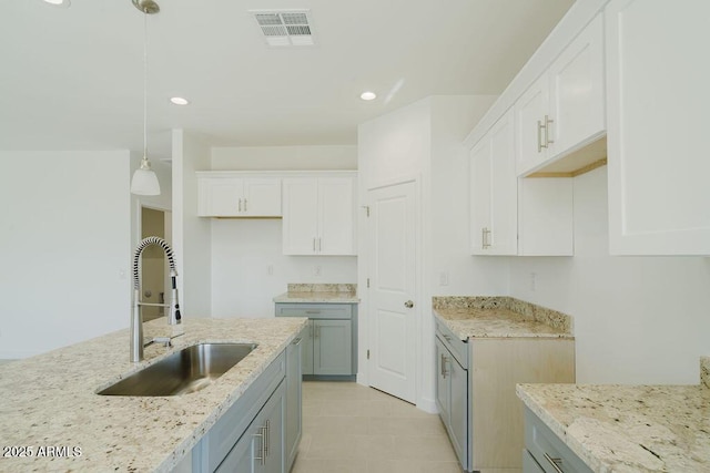 kitchen with hanging light fixtures, sink, light stone counters, and white cabinetry