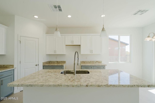 kitchen featuring white cabinetry, an island with sink, light stone countertops, pendant lighting, and sink