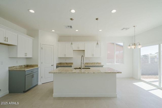 kitchen featuring sink, hanging light fixtures, light stone countertops, an island with sink, and white cabinets