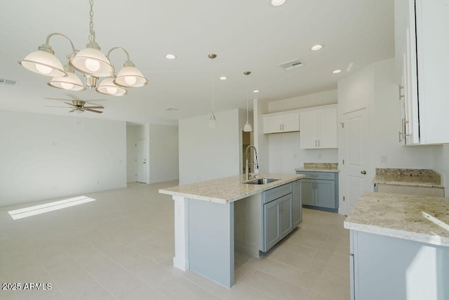 kitchen with a center island with sink, ceiling fan, hanging light fixtures, white cabinets, and sink