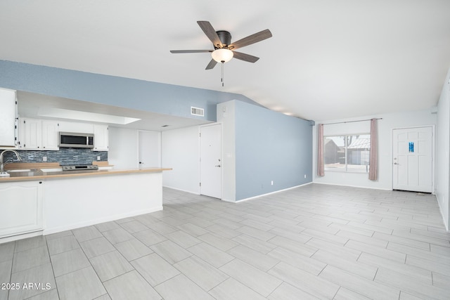 unfurnished living room with lofted ceiling, a sink, visible vents, a ceiling fan, and baseboards