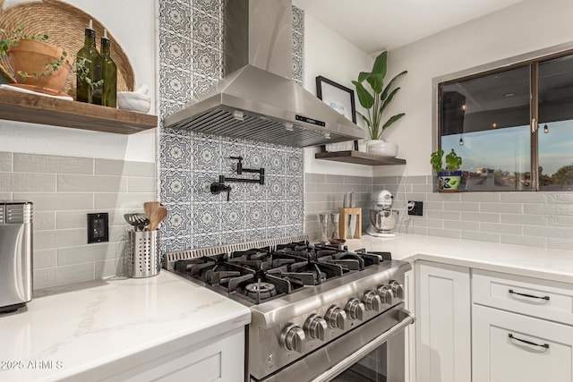 12866 W Orange Dr, Litchfield Park, AZ 85340 - kitchen featuring wall chimney range hood, stainless steel gas range oven, open shelves, decorative backsplash, and white cabinets