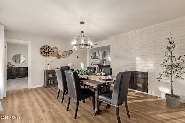 12866 W Orange Dr, Litchfield Park, AZ 85340 - dining space with light wood-style flooring, a chandelier, a fireplace, brick wall, and baseboards