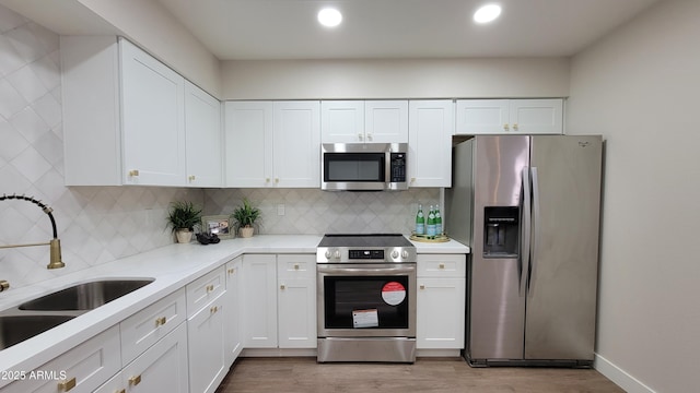 kitchen with sink, white cabinetry, tasteful backsplash, light wood-type flooring, and appliances with stainless steel finishes