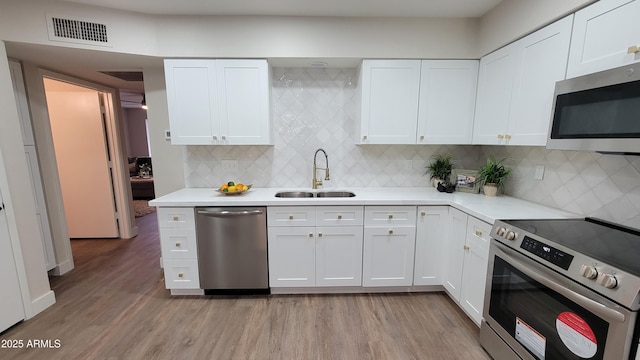 kitchen with stainless steel appliances, sink, white cabinets, and light hardwood / wood-style flooring