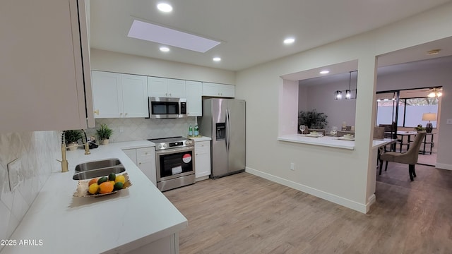 kitchen with white cabinetry, decorative light fixtures, stainless steel appliances, and light wood-type flooring