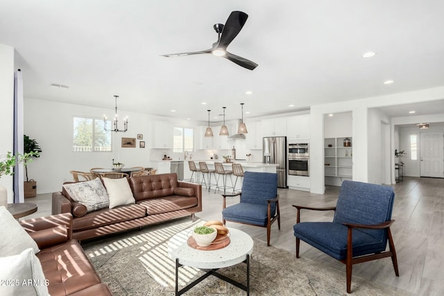 living room featuring light wood-type flooring and ceiling fan with notable chandelier