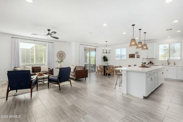 kitchen with a kitchen bar, white cabinetry, hanging light fixtures, sink, and a kitchen island