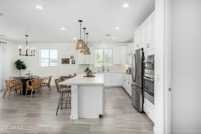 kitchen with stainless steel fridge, hanging light fixtures, sink, white cabinetry, and a kitchen island