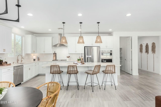 kitchen featuring appliances with stainless steel finishes, hanging light fixtures, sink, a kitchen island, and wall chimney exhaust hood