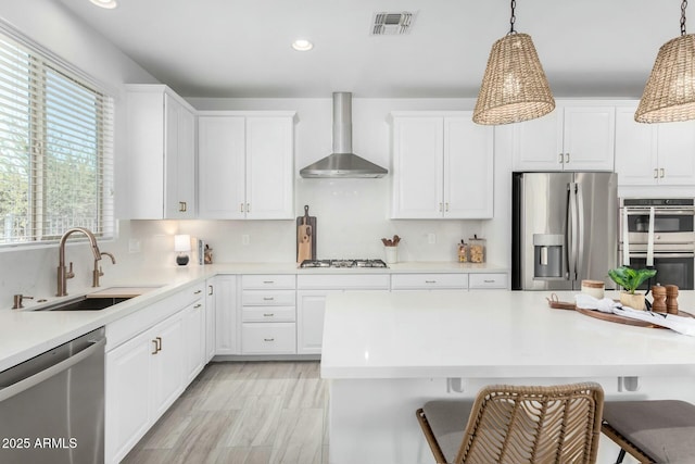 kitchen featuring a kitchen bar, pendant lighting, wall chimney range hood, and appliances with stainless steel finishes