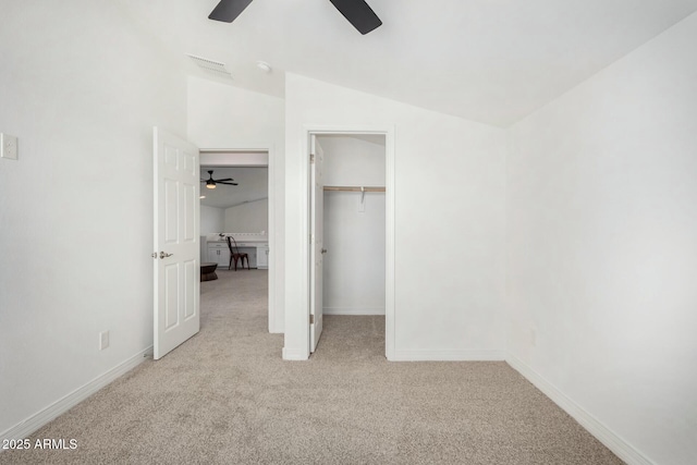 unfurnished bedroom featuring ceiling fan, a spacious closet, light carpet, and vaulted ceiling