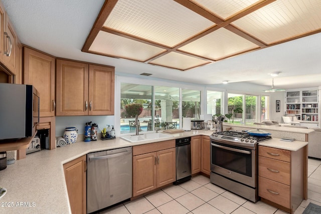 kitchen with appliances with stainless steel finishes, light countertops, a peninsula, and a sink
