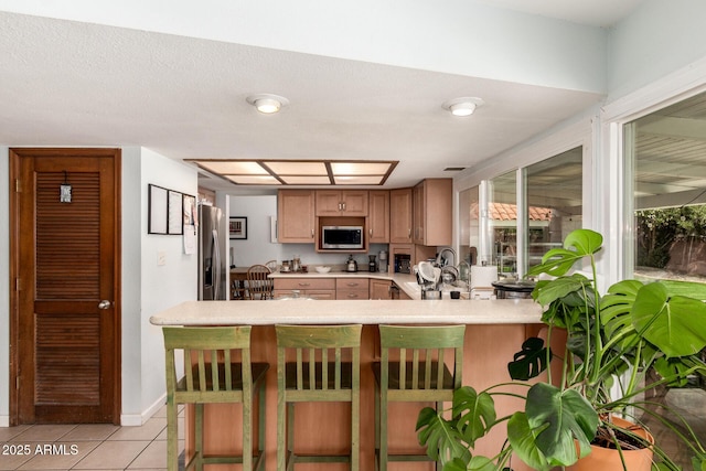 kitchen featuring a kitchen bar, stainless steel appliances, a peninsula, light countertops, and light tile patterned floors