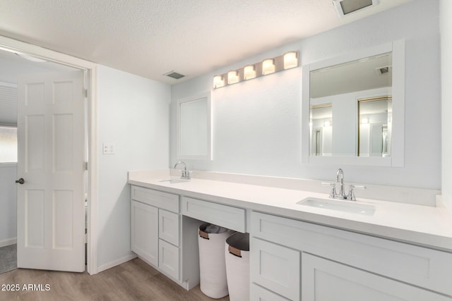 full bath with visible vents, a textured ceiling, wood finished floors, and a sink