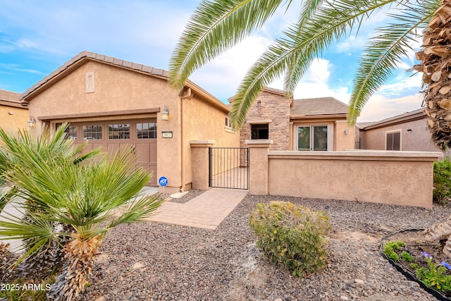 view of front of home with fence, stone siding, a garage, stucco siding, and a gate
