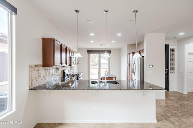 kitchen with a sink, appliances with stainless steel finishes, dark stone countertops, and a peninsula