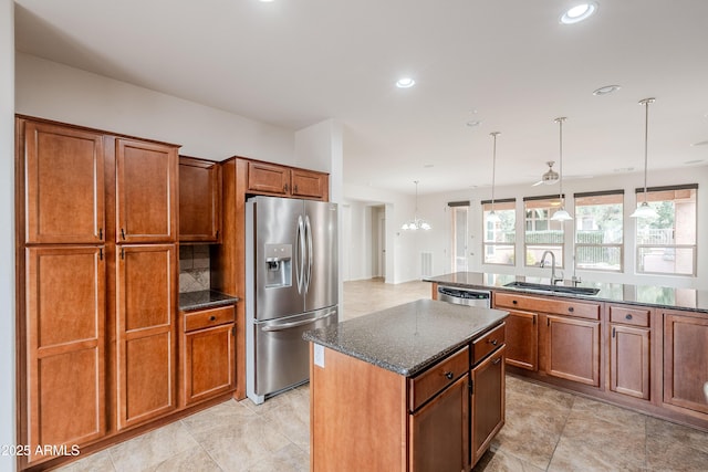 kitchen with a sink, brown cabinetry, dark stone countertops, stainless steel appliances, and a kitchen island