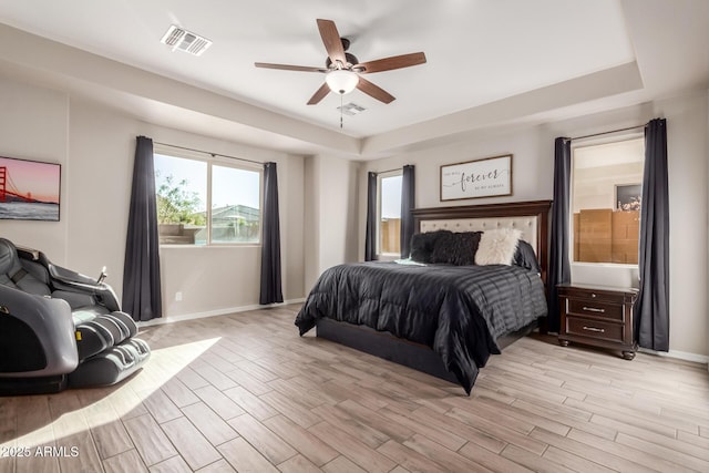 bedroom featuring ceiling fan, light wood-type flooring, and a tray ceiling