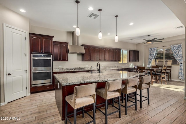 kitchen featuring ceiling fan, sink, wall chimney exhaust hood, decorative light fixtures, and appliances with stainless steel finishes