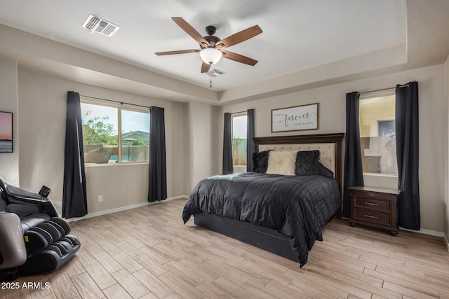 bedroom featuring ceiling fan, a tray ceiling, and light hardwood / wood-style flooring