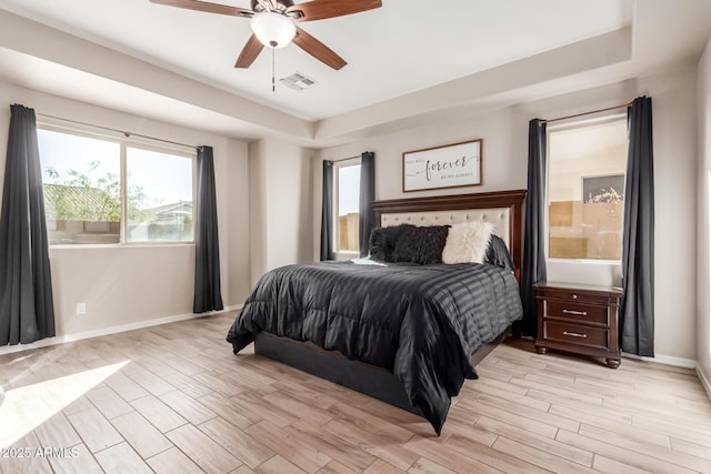 bedroom featuring light wood-type flooring, a raised ceiling, and ceiling fan