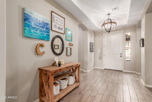 foyer with a raised ceiling and a notable chandelier