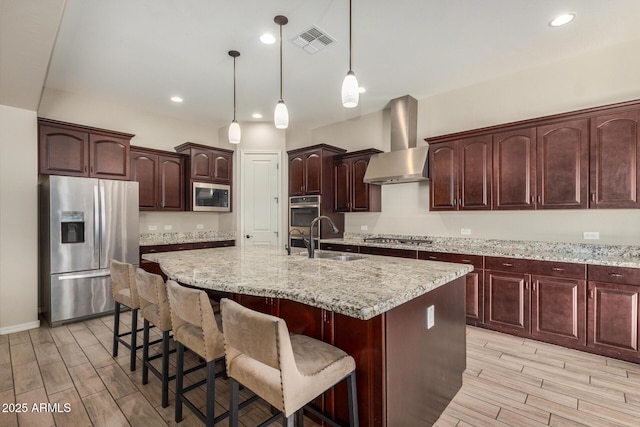 kitchen with sink, wall chimney exhaust hood, an island with sink, pendant lighting, and appliances with stainless steel finishes