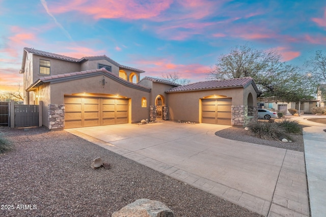 mediterranean / spanish house with stone siding, stucco siding, concrete driveway, and a garage