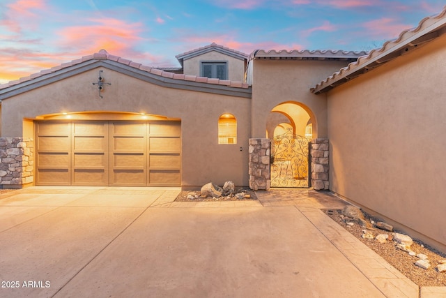 mediterranean / spanish house featuring stucco siding, concrete driveway, an attached garage, and a tiled roof