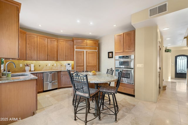 kitchen with stainless steel double oven, sink, a kitchen island, a breakfast bar, and paneled refrigerator