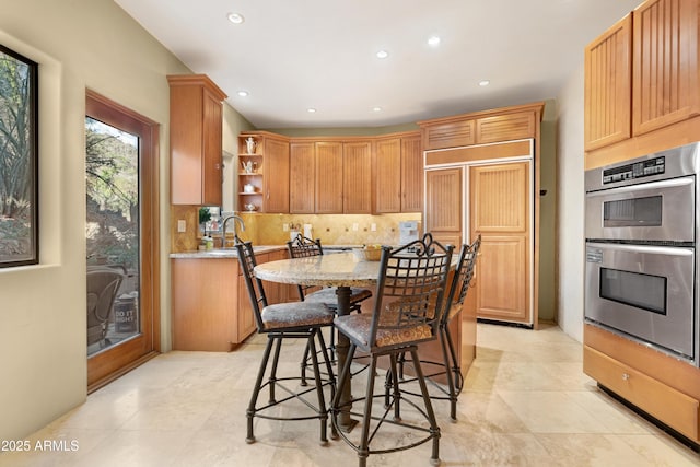 kitchen with tasteful backsplash, a kitchen breakfast bar, paneled built in fridge, light stone counters, and double oven