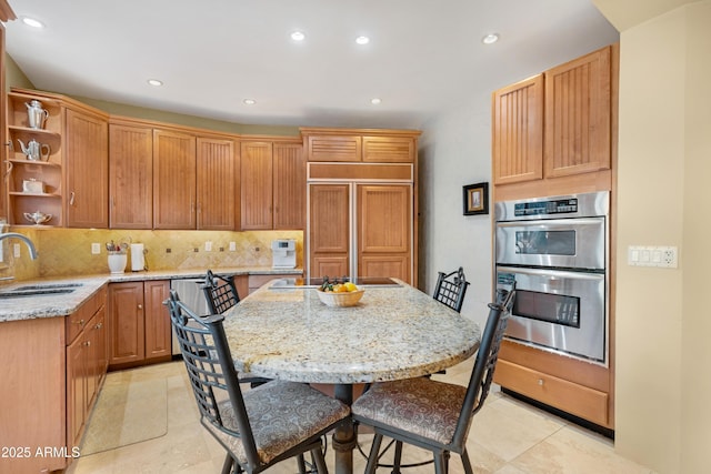 kitchen featuring sink, a kitchen island with sink, paneled refrigerator, and light stone counters