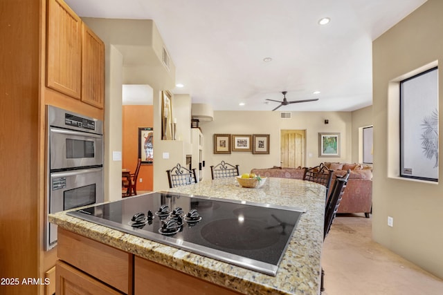 kitchen with black electric cooktop, double oven, ceiling fan, and light stone counters