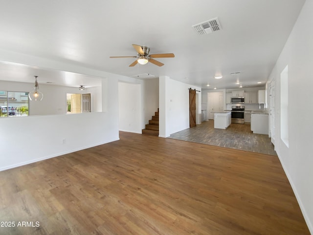 unfurnished living room with visible vents, a sink, wood finished floors, a barn door, and ceiling fan