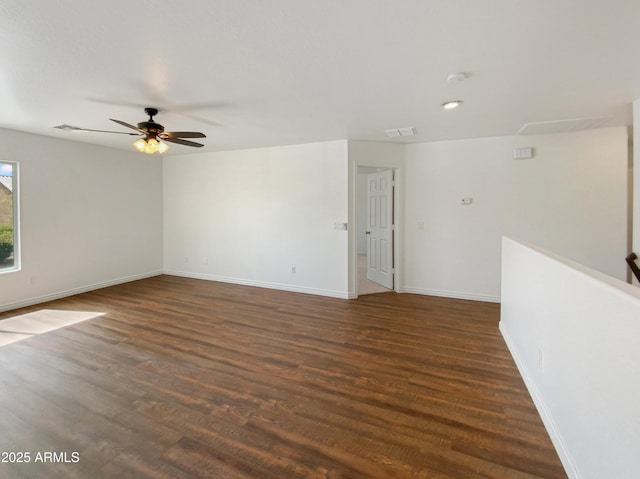 empty room featuring visible vents, a ceiling fan, baseboards, attic access, and dark wood-style flooring