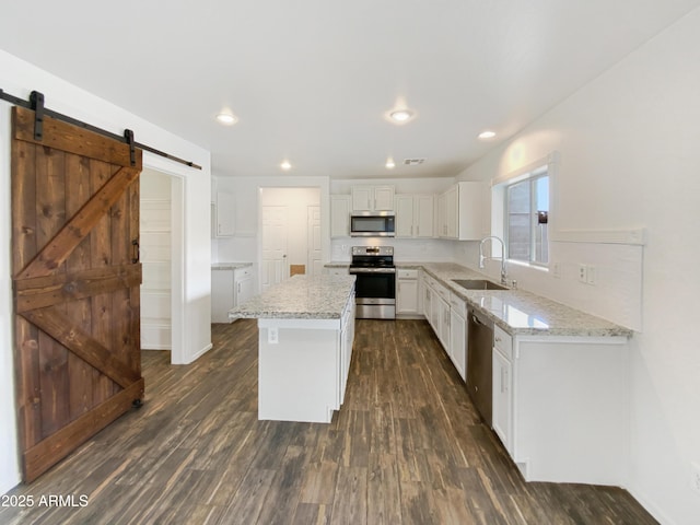 kitchen featuring a sink, a barn door, appliances with stainless steel finishes, white cabinets, and dark wood-style flooring