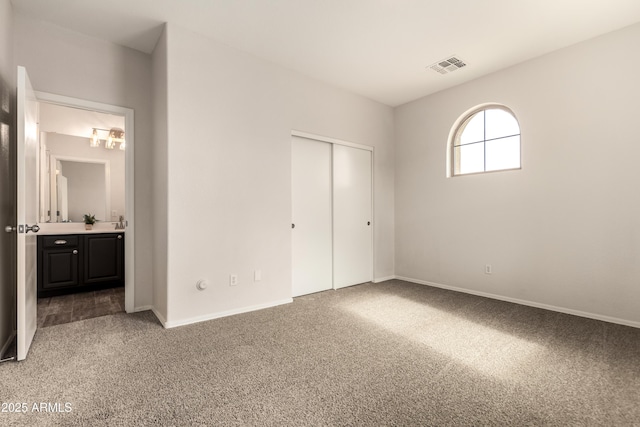 unfurnished bedroom featuring ensuite bathroom, a closet, and carpet flooring