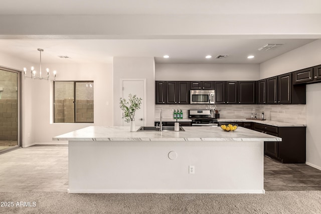 kitchen with pendant lighting, sink, stainless steel appliances, tasteful backsplash, and a center island with sink