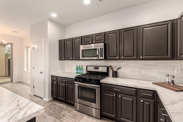 kitchen featuring tasteful backsplash, appliances with stainless steel finishes, an inviting chandelier, and light stone counters