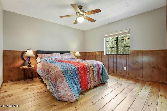 bedroom with light wood-type flooring, wainscoting, and wood walls