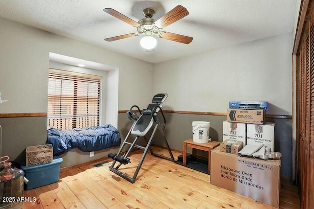 workout room with ceiling fan, a textured ceiling, and wood finished floors