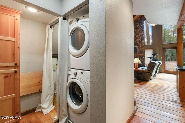 laundry area with light wood-style flooring, stacked washer / drying machine, and a textured wall