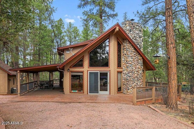 rear view of house with stone siding, a chimney, and a deck