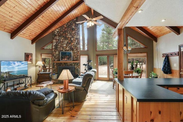 living room with light wood finished floors, a stone fireplace, high vaulted ceiling, wooden ceiling, and beamed ceiling