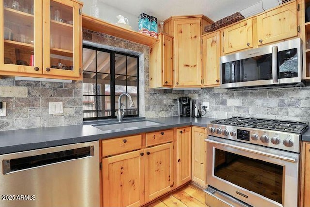 kitchen with stainless steel appliances, a sink, tasteful backsplash, dark countertops, and glass insert cabinets