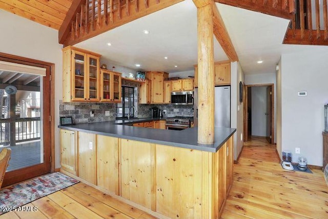 kitchen featuring dark countertops, appliances with stainless steel finishes, glass insert cabinets, and a peninsula